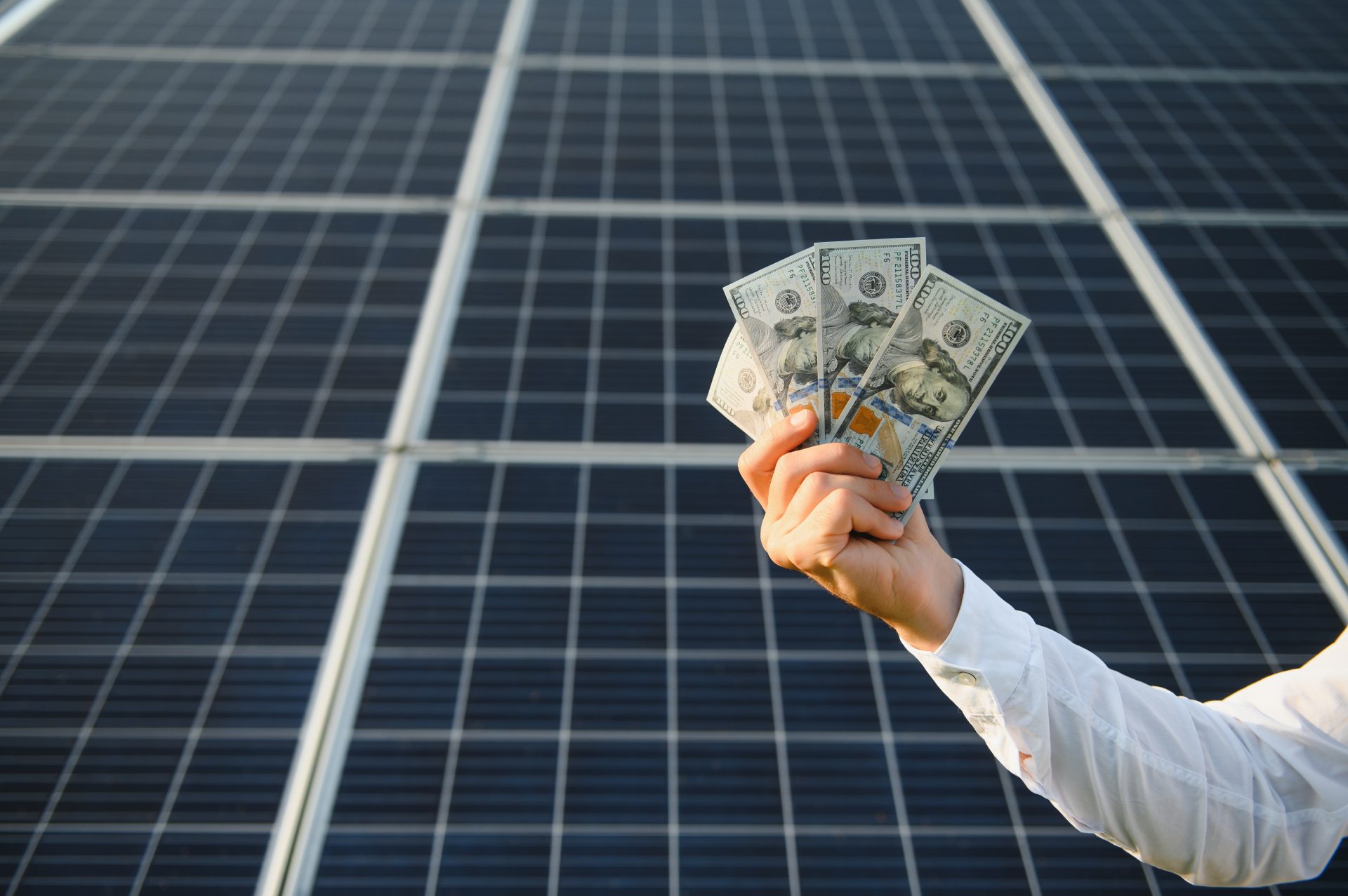 Hand holding money in front of solar panels representing business energy cost savings